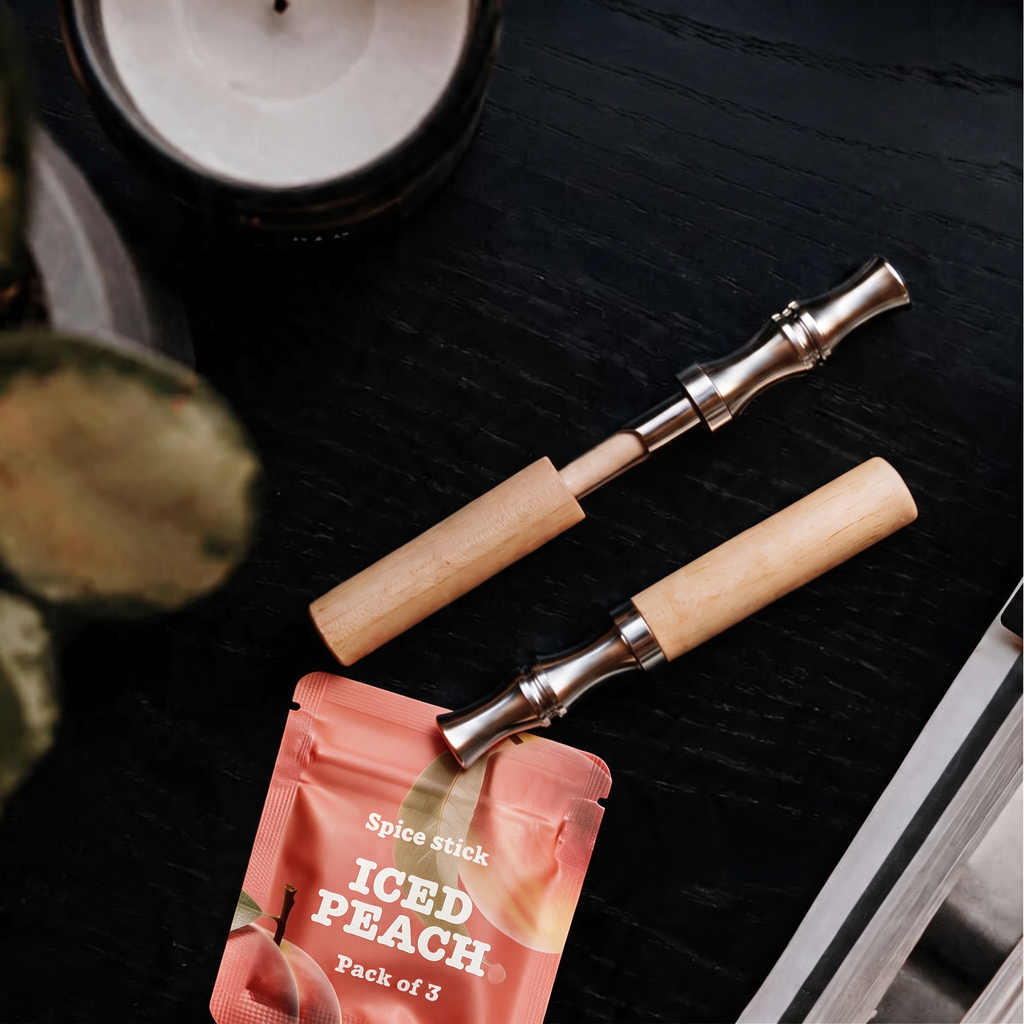 Zwei QuitAir Sticks aus Holz mit Edelstahl-Mundstück neben einem Iced Peach Aroma-Päckchen